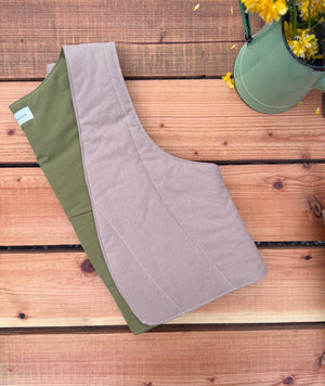 Brown and green quilted vest  on a wooden surface with flowers in a pot in the background