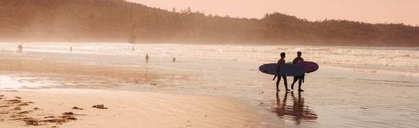 Two people with surfboards walking on a beach at sunset.