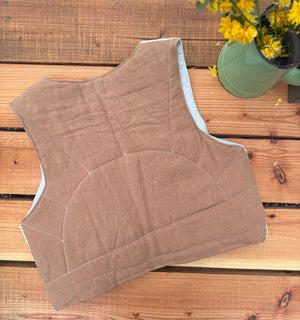 Brown quilted vest on a wooden surface with a potted plant in the background