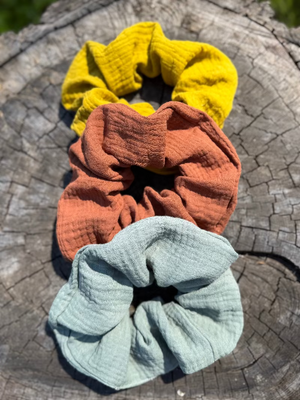 Three fabric scrunchies in yellow, orange, and blue on a wooden surface