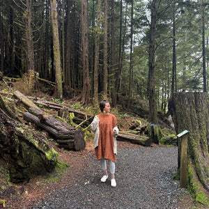 Person walking on a path through a forest with tall trees and logs.