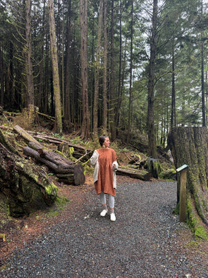 Person walking on a path through a forest with tall trees and logs.