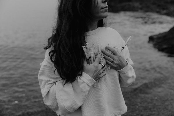 Woman holding handful of syringes close to her chest, standing by the water