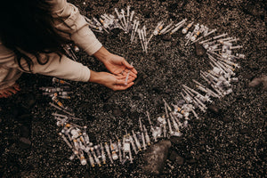 needles and vials spread out in a heart shop on a beach. Woman holding hands out.