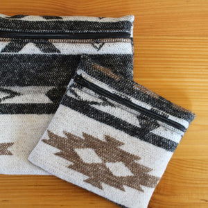 May include: Two zippered pouches with a black, white and brown geometric pattern. The larger pouch is on the bottom and the smaller pouch is on top.